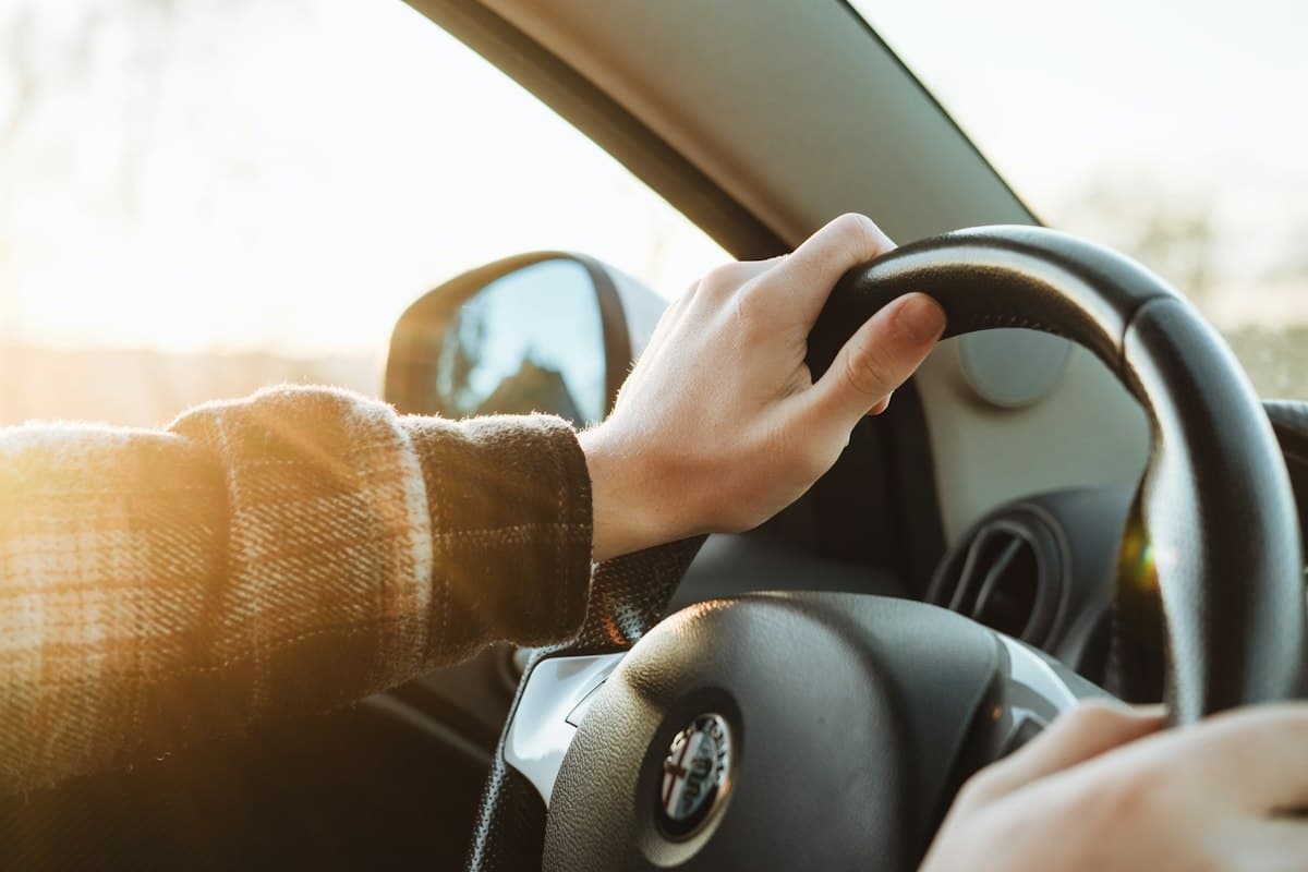 Hands resting on a car steering wheel in daylight